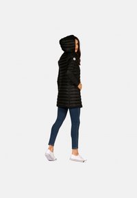 Manteau d'hiver noir en duvet avec un design matelassé, capuche et poches zippées, associé à un jean skinny bleu et des baskets blanches.