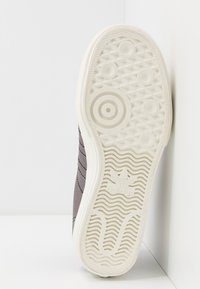 Brun sneaker sula med textur gummi i vitt, med cirkulära mönster och en framträdande varumärkeslogo vid hälen. Släta kanter, inga dekorerade detaljer.