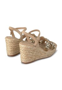 Sandali a zeppa beige con suola in paglia intrecciata e accenti decorativi in pietra. Design con cinturino regolabile e finitura morbida simile alla scamosciata.