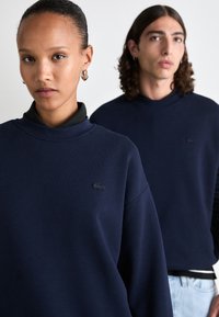 Dunkelblaue Sweatshirts mit hohem Kragen und langen Ärmeln, aus einem strukturierten Stoff und mit dezentem Lacoste-Logo auf der Brust.