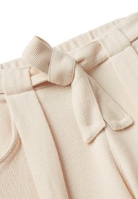 Nahaufnahme von beigen, gerippten Strickhosen mit einem elastischen Bund und einem Stoffgürtel, der zu einer Schleife gebunden ist.