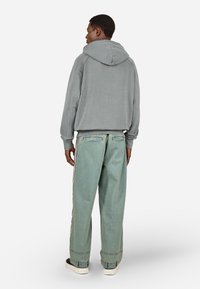 Pelēks sporta krekls ar brīvu piegriezumu un kapuci ar auklu, apvienots ar plašām gaiši zilām džinsu biksēm ar sānu svītrām un apgrieztiem apakšējiem malām.