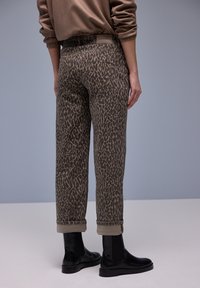Ruskeat leopardikuvioiset housut, joissa rento istuvuus, käännetyt lahkeet ja vyötäröllä etiketti, yhdistetty mustiin nilkkureihin.