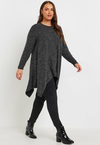 Szara tunika z długim rękawem, o asymetrycznym dole, wykonana z miękkiego materiału, połączona z dopasowanymi czarnymi spodniami i błyszczącymi botkami do kostek.