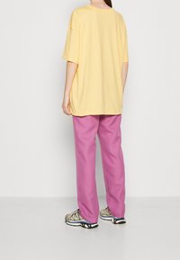 Camiseta amarilla de gran tamaño, pantalones rosas y zapatillas con estampado. Tejido suave, corte relajado, mangas cortas y escote redondo.