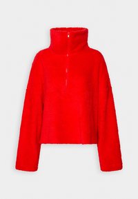 Czerwona, skrócona bluza polarowa z wysokim kołnierzem i zamkiem błyskawicznym do jednej czwartej długości. Posiada luźne, długie rękawy i miękką teksturę.