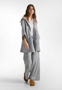 Grijze hoodie met een oversized pasvorm, voorzien van zakken en een trekkoord. Gepaard met wijde grijze sweatpants en bruine, zachtzolen schoenen.