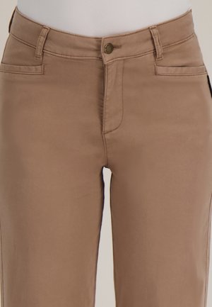 Close-up van beige broek met knoop aan de voorkant, ritssluiting en riemlussen, die het bovenbeen en het taillegebied toont.