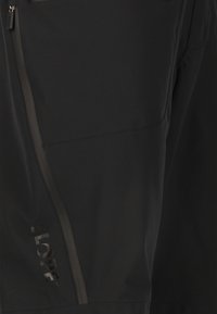 Svarta softshell-byxor med sidoficka med dragkedja, slät textur och ordet "SLOPE" tryckt med en subtil metallisk finish.