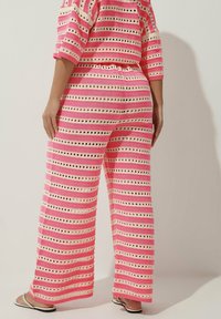 Różowy zestaw dzianinowy w paski z ażurowymi detalami. Luźny top ma szerokie rękawy, a spodnie są szerokie i mają elastyczny pasek w talii.