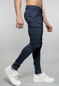 Tmavě modré úzké kalhoty z texturované látky s jedním předním kapsou a hladkým pasovým lemem, doplněné bílými teniskami.