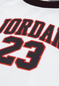 Valge spordisärk, millel on mustades ja punastes tähtedes "JORDAN" ning must number "23", mille kontuur on punane; valmistatud võrkkangast.