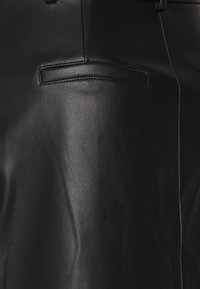 Nära bild av slät svart läderplagg som visar en sydd welt-ficka och sömdetaljer.