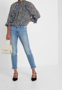 Blusa a righe bianco e nero con volants blu, jeans azzurri, e tacchi neri con dettagli in perle, abbinati a una borsa color crema.