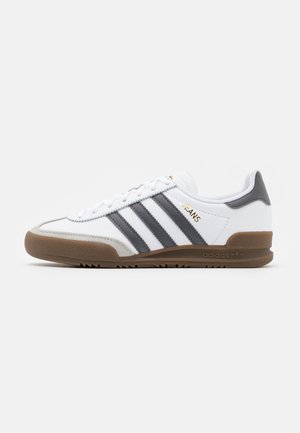 Baskets blanches Adidas avec des bandes noires, une semelle en gomme et le texte doré "Jeans" sur le côté, vues de l'intérieur.