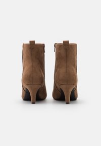 Bottes courtes en daim marron avec un talon effilé, dotées d'une fermeture éclair latérale et de coutures décoratives le long des coutures.