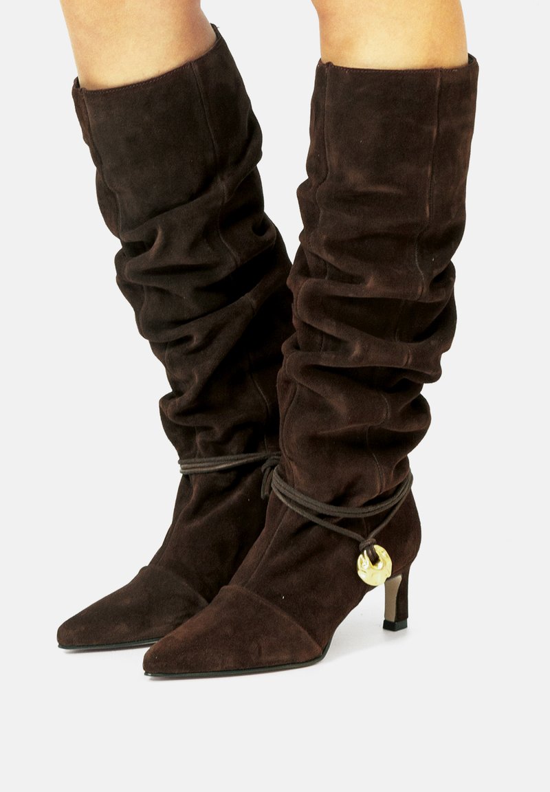 Botas altas de ante marrón con textura recogida, punta afilada y un tacón bajo. Presentan un acento decorativo de hardware dorado y un cierre atado.