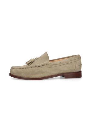 Beige suède loafer met kwastjes, stikseldetails en een bruine houten zool, zijaanzicht op een witte achtergrond.