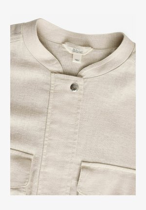 Jasno beżowa lniana koszula z okrągłym kołnierzykiem, zapięciem na napy i dwiema przednimi kieszeniami o subtelnej fakturze.