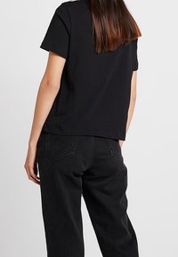 Schwarzes Baumwoll-T-Shirt mit kurzen Ärmeln, lockerer Passform und rundem Halsausschnitt, kombiniert mit hochgeschnittenen schwarzen Jeans mit Gesäßtaschen.