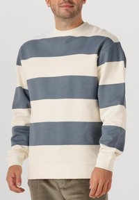 Sweatshirt en coton rayé avec de larges bandes horizontales alternées navy et crème, col rond, et manches longues avec des poignets côtelés.