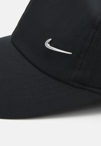 Casquette noire en tissu avec une visière incurvée. Présente un élégant logo en argent de la marque Nike sur le devant et des détails de couture subtils.