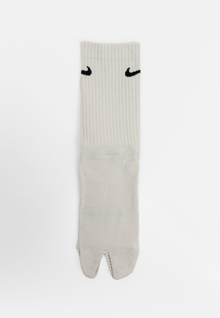 Chaussette blanche à orteils séparés avec une section supérieure côtelée et deux petits logos swoosh noirs près de la cheville.