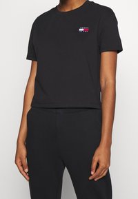 T-shirt nera cropped in cotone con scollo rotondo. Presenta un piccolo logo multicolore sul petto. Abbinata a pantaloni neri.