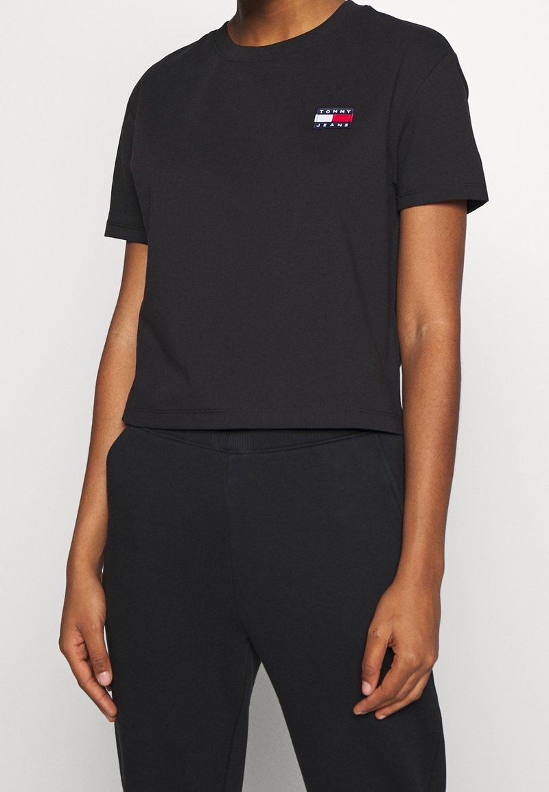 T-shirt nera cropped in cotone con scollo rotondo. Presenta un piccolo logo multicolore sul petto. Abbinata a pantaloni neri.