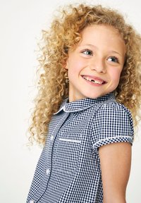 Marinblå och vit gingham-skjorta med korta ärmar och krage, med en ficka och knäppning, bärs av ett barn med lockigt hår.