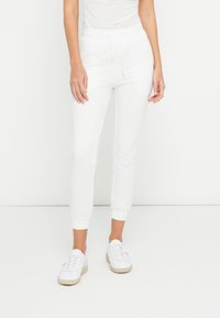 Calças jogging de algodão branco com cintura elástica e punhos nas pernas, apresentando bolsos laterais e corte descontraído, combinadas com ténis brancos.