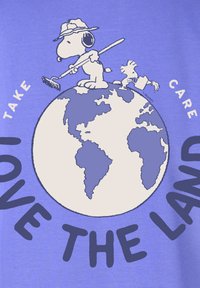 T-shirt viola chiaro con una grafica di un cane e un uccello su un globo, con il testo "AMARE LA TERRA" e "PRENDERSI CURA" in lettere grasse e scure.