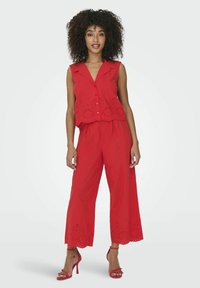 Completo rosso a due pezzi composto da un top senza maniche con dettagli a occhiello e pantaloni a gamba larga a vita alta, abbinato a tacchi rossi.