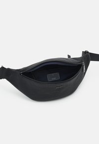 Black textured leather fanny pack with a zippered opening and adjustable strap, featuring a plain interior and a brand label inside.