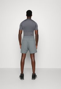Camisa atlética cinza de mangas curtas, combinada com calções cinza. Modelo a usar sapatilhas desportivas pretas. Fundo simples.