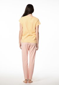 Lichtgele top met korte mouwen gecombineerd met roze broek met een verspreid blauw stippenpatroon. Zacht materiaal, losse pasvorm, broek tot de enkels.