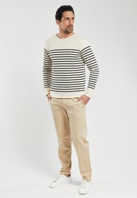 Maglione a righe in crema e blu navy, abbinato a pantaloni beige e sneakers bianche. Il maglione ha maniche lunghe e scollatura rotonda.