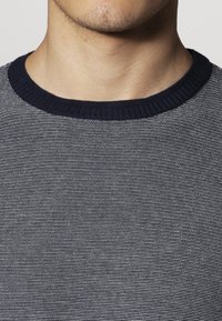 Navy en witte gestreepte gebreide trui met een geribbelde ronde hals, textuur stof en nauwsluitend ontwerp. Glad textuur en subtiele patroondetails.
