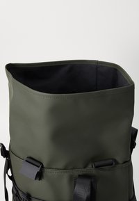 Grüner wasserdichter Rucksack mit rechteckiger Öffnung, genähten Kanten und schwarzem Futter; ausgestattet mit verstellbaren Trägern und einem Schnallenverschluss.