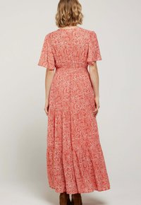 Robe maxi rouge avec un motif paisley blanc, manches courtes, taille élastique et conception à volants. Tissu doux avec une apparence fluide.