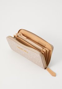 Beige plånbok med en slät ytfinish och präglat logomönster, ett dragkedjesystem runtom och flera kortfack inuti.