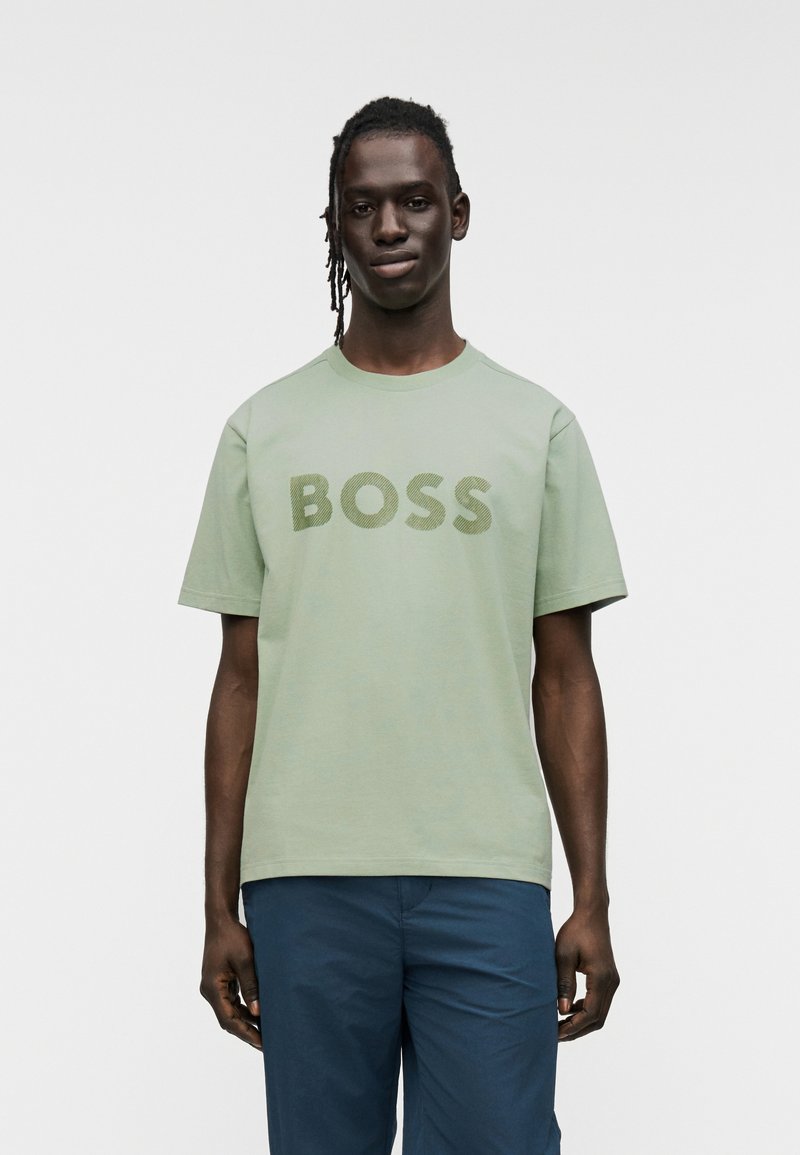 Ανοιχτό πράσινο βαμβακερό T-shirt με τη λέξη "BOSS" σε πιο σκούρα πράσινα γράμματα. Κοντά μανίκια και στρογγυλή λαιμόκοψη.