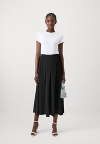 Hvid kortærmet t-shirt parret med en sort plisseret midi-nederdel. Modellen holder en lille lyseblå taske. Klare hæle fremhæver outfittet.