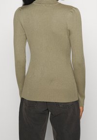 Żebrowany sweter w oliwkowym kolorze z golfem i długimi rękawami, z delikatnym marszczeniem na ramionach i dopasowanym krojem.