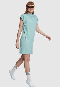 Vestido de algodón verde menta, de manga corta y con un corte relajado. Combinado con zapatos blancos tipo slip-on y calcetines a rayas por el tobillo. Destaca por su diseño sencillo.