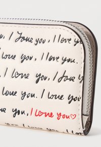 Πορτοφόλι με φερμουάρ από μαλακό κρέμ συνθετικό δέρμα, με επαναλαμβανόμενο μαύρο χειρόγραφο κείμενο και κόκκινο στοιχείο "Σ' αγαπώ". Λεπτομερής ραφή κατά μήκος των άκρων.