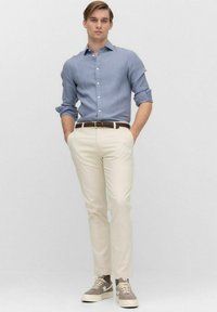 Jasnoniebieska koszula zapinana na guziki, beżowe dopasowane spodnie, ciemny pleciony pasek, szare zamszowe trampki. Gładki materiał, klasyczny kołnierzyk, podwinięte rękawy.