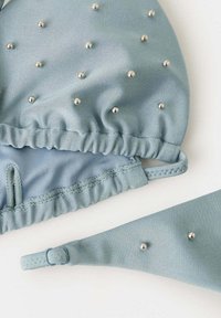 Bikini bleu clair avec ornements en perles argentées et bretelles réglables, présenté sur fond blanc.