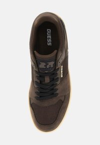 Sneaker marrone caratterizzato da una combinazione di materiali lisci e testurizzati, con lacci neri, dettagli in rete e una suola in gomma bianca con branding sulla linguetta.