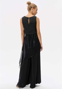 Zwarte jurk met een aansluitende lijfje, transparante overlay met een asymmetrische zoom en een keyhole rugdetail. Gemaakt van gladde stof met een vloeiende silhouet.